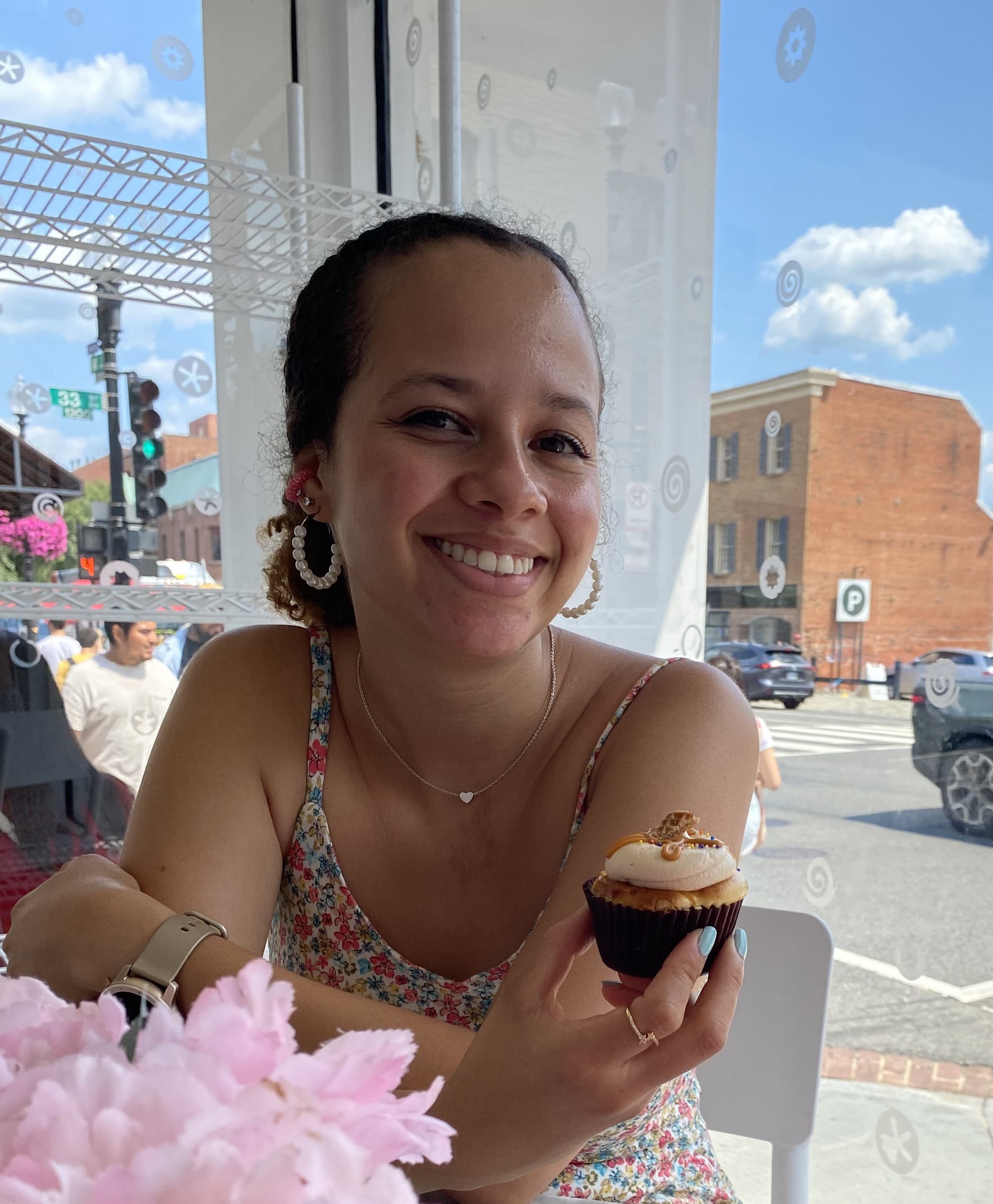 Cami smiling at a café holding a cupcake, sunny day outside